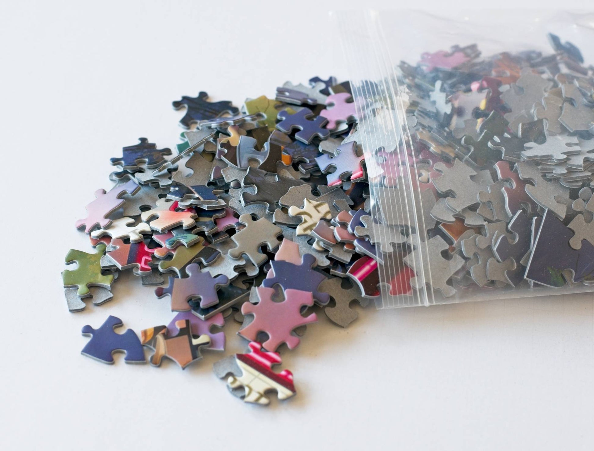 Pile of assorted puzzle pieces with a clear plastic bag on a white background