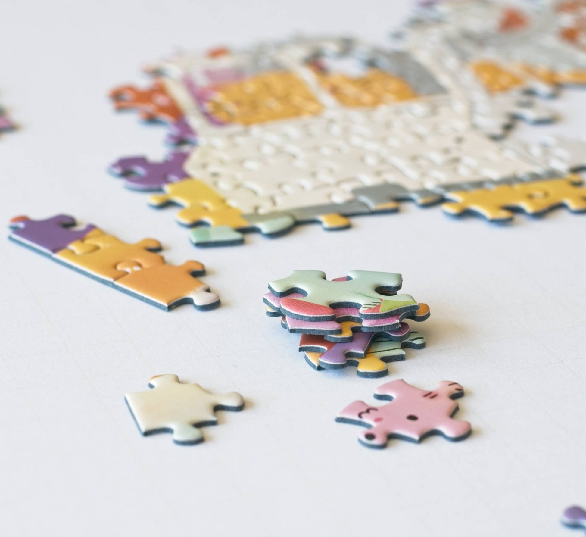 Colorful puzzle pieces stacked with a partially completed puzzle in the background on a white surface