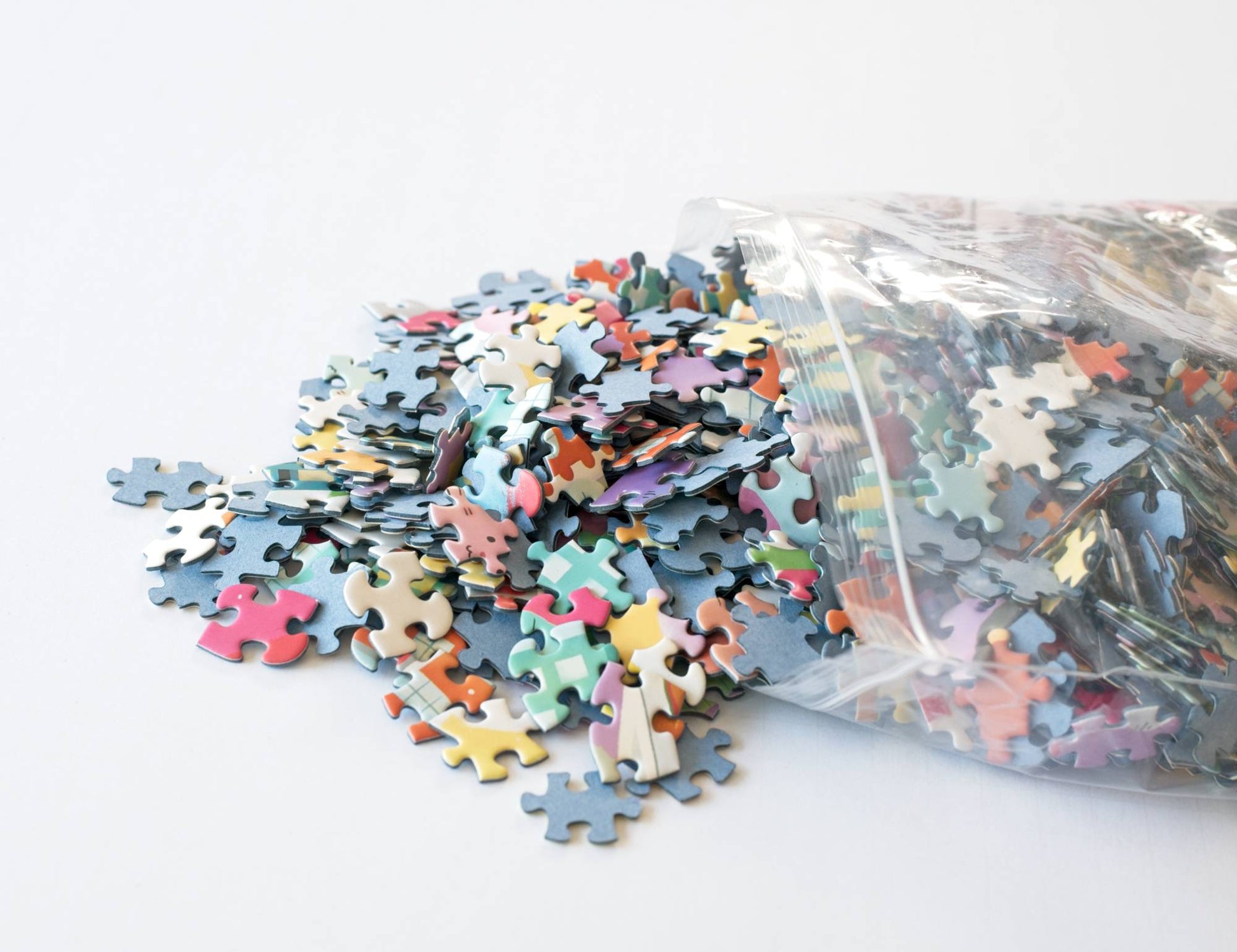Colorful puzzle pieces spilling out of a clear plastic resealable bag on a white background