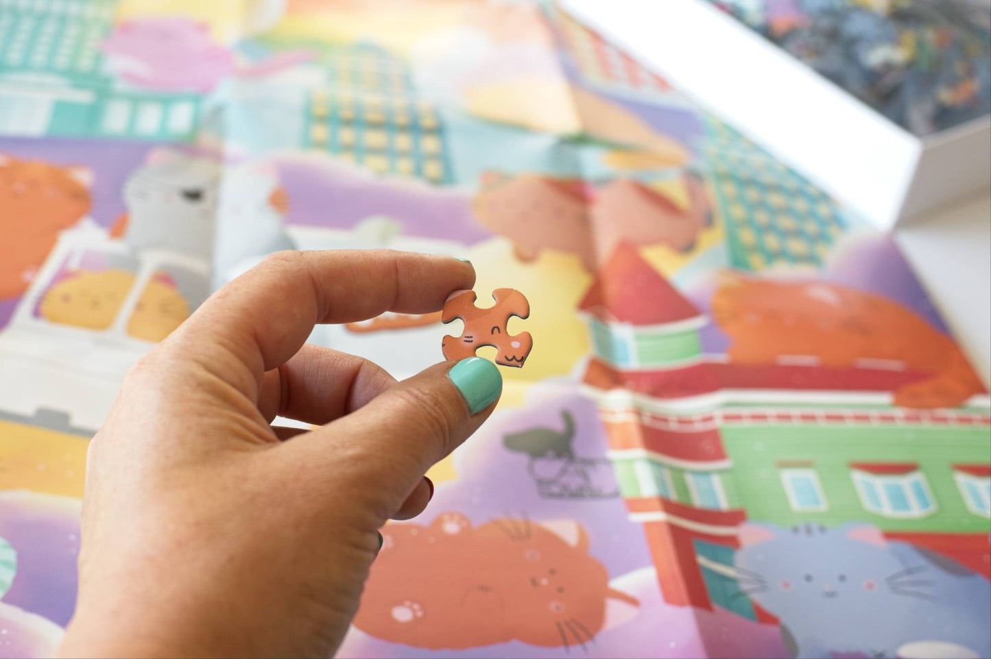 Hand holding a puzzle piece in front of a colorful poster with cats and a puzzle box in the background