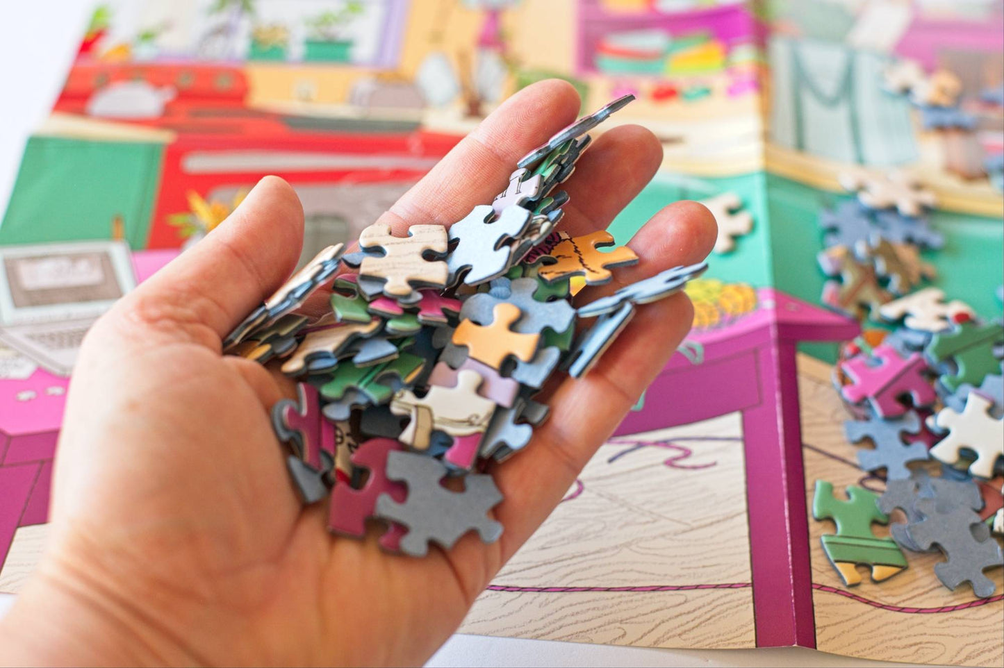 Hand holding a pile of puzzle pieces with a colorful image and more puzzle pieces in the background
