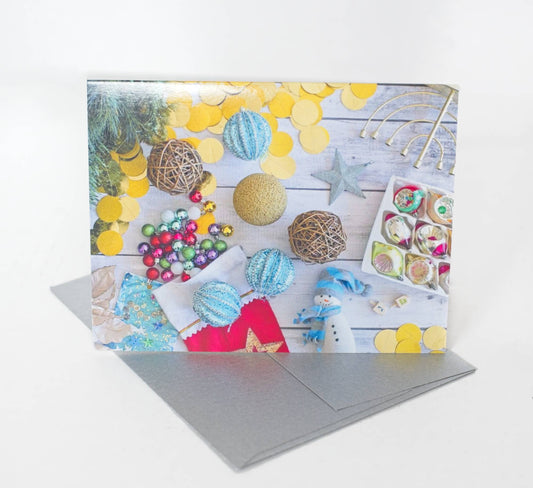 A photo of a greeting card that features a flatlay photo of a beachy rustic table scattered with ornaments and jewish and christian winter holiday items. The card sits on a silver envelope