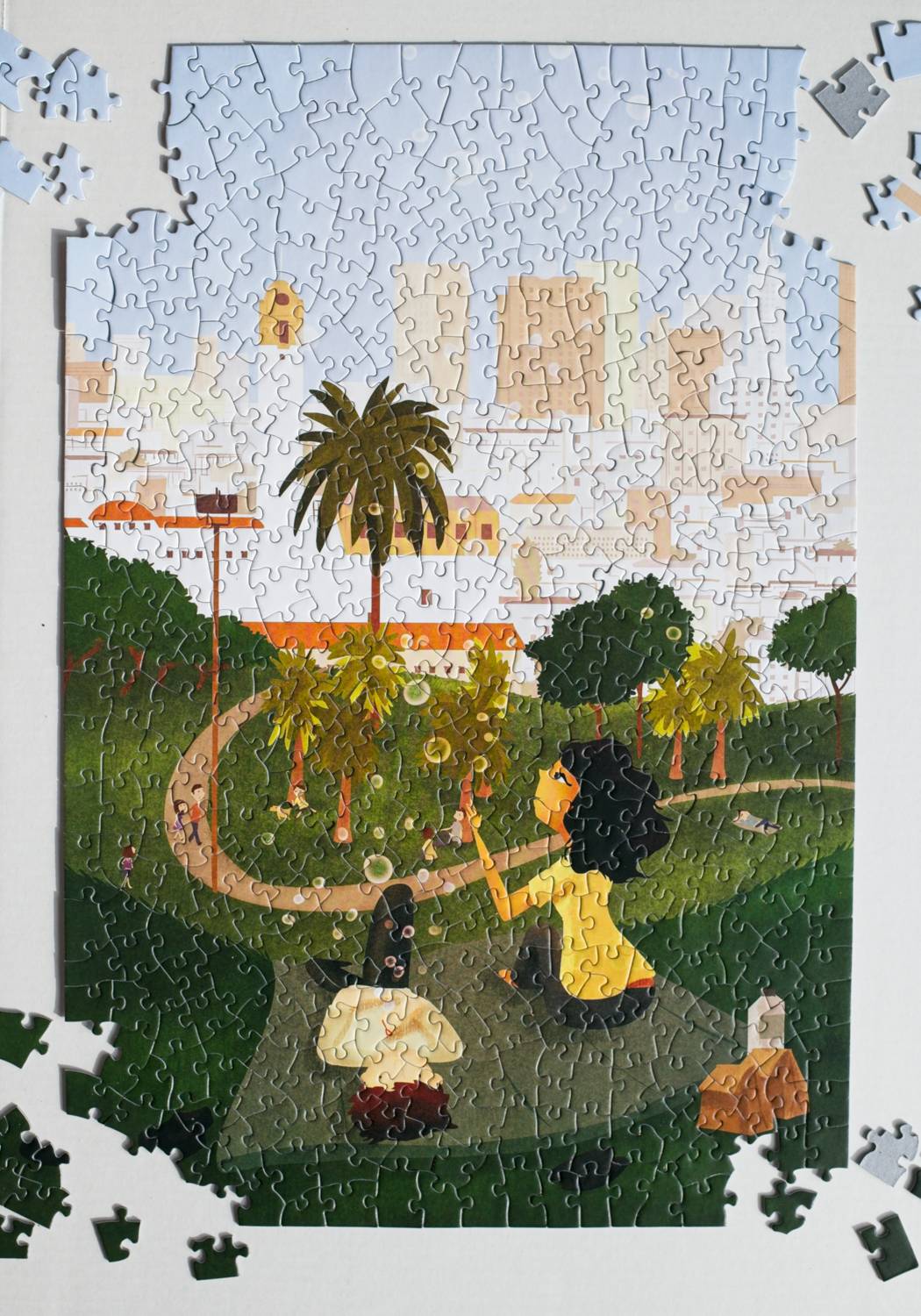 Jigsaw puzzle with a completed section showing a two people blowing bubbles on picnic in a park with palm trees and the San Francisco skyline in the background.