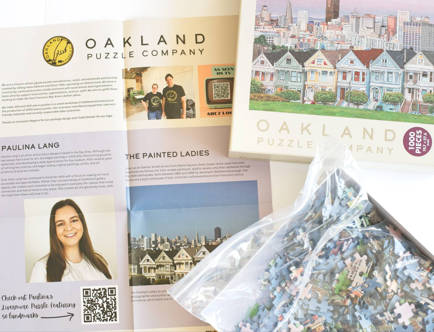 Oakland Puzzle Company packaging with a puzzle bag holding jigsaw puzzle pieces and promotional material.