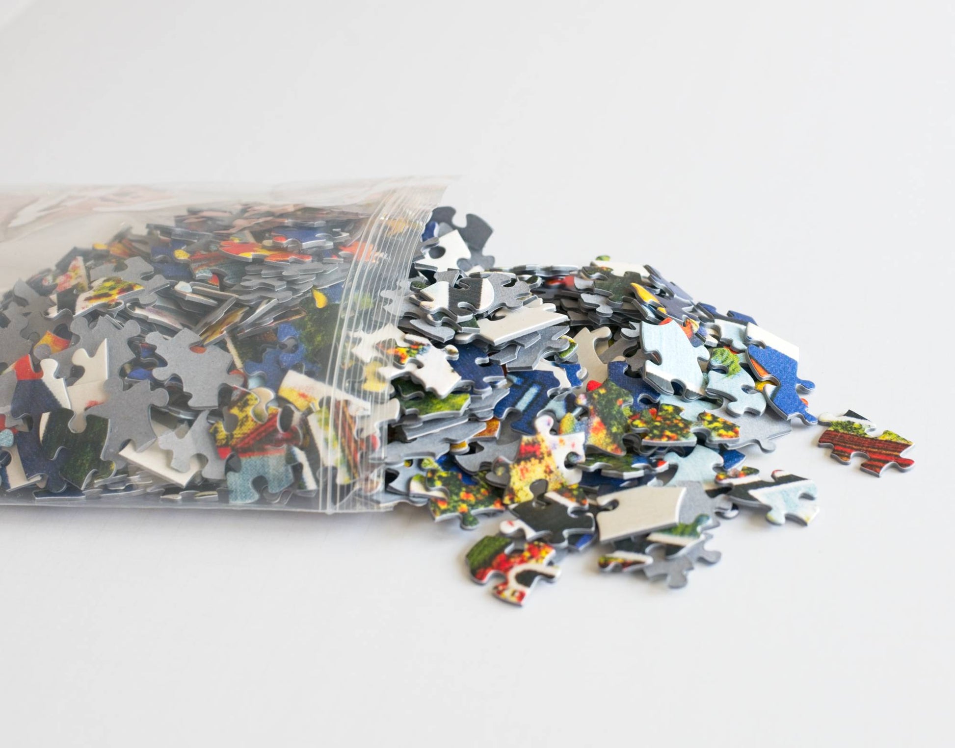 A resealable plastic bag spilling colorful puzzle pieces out onto a white surface.