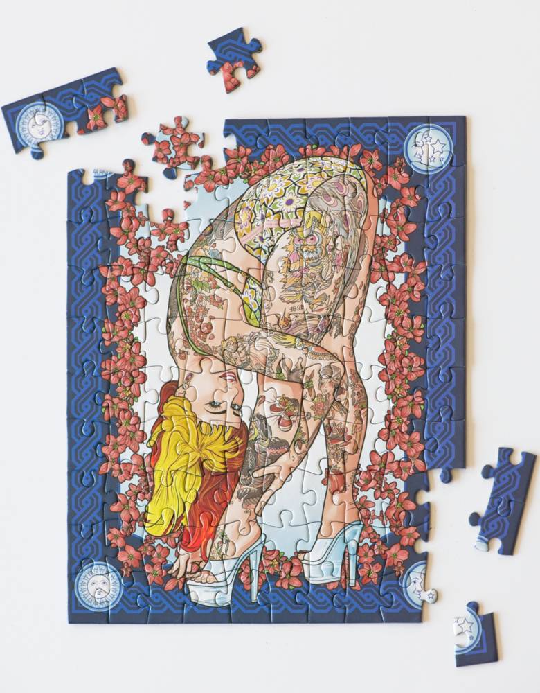 A completed jigsaw puzzle showing a tattooed woman in a yellow top and white heels, framed by red flowers on a blue border, with several loose puzzle pieces around it on a white background.