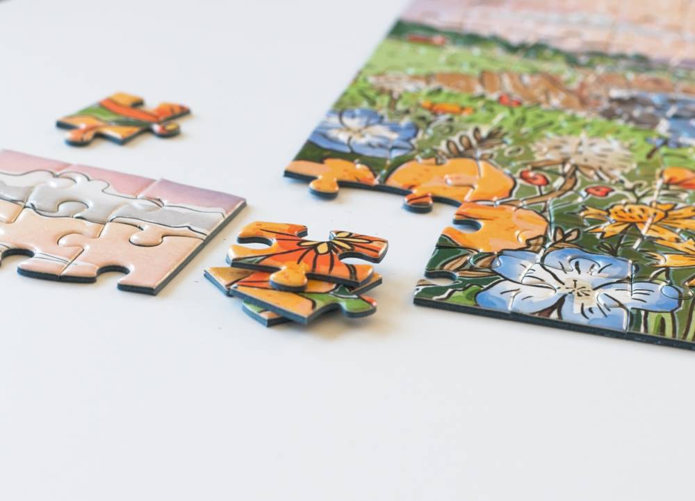 A close-up of a colorful floral jigsaw puzzle on a white surface, with several loose puzzle pieces scattered around it.