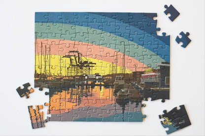 A nearly completed jigsaw puzzle showing a colorful harbor scene with cranes and reflections, surrounded by several loose puzzle pieces on a plain white background.