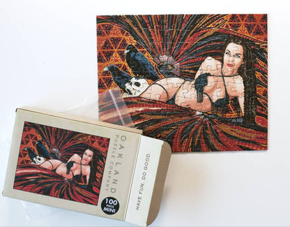 A 100-piece mini jigsaw puzzle and its packaging box, both featuring a gothic pin-up style illustration of a woman in a black bikini against a red and black fanburst background.