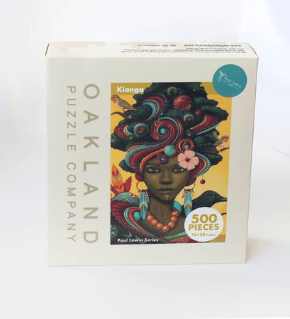 A box branded Oakland Puzzle Company with a painted image of an ornately dressed Afrofuturist woman with birds, butterflies, and feathers titled Kianga Paul Lewin Series