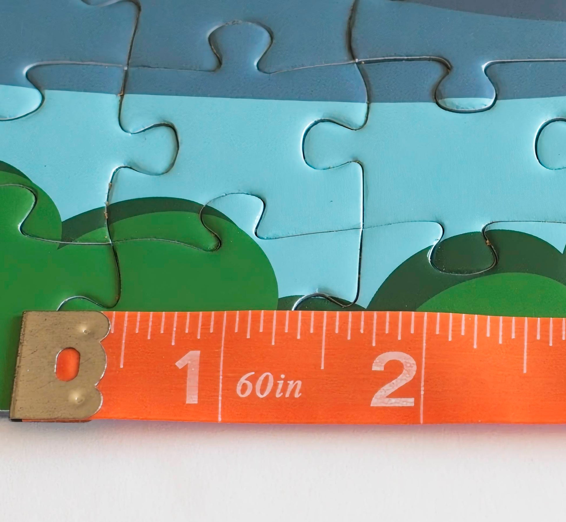 A measuring tape laid over a section of a jigsaw puzzle showing that hte pieces are about 1.5 inches