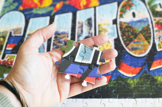 A hand hovering over a colorful jgsaw puzzle holding 4 puzzle pieces, which cover most of the fingers.