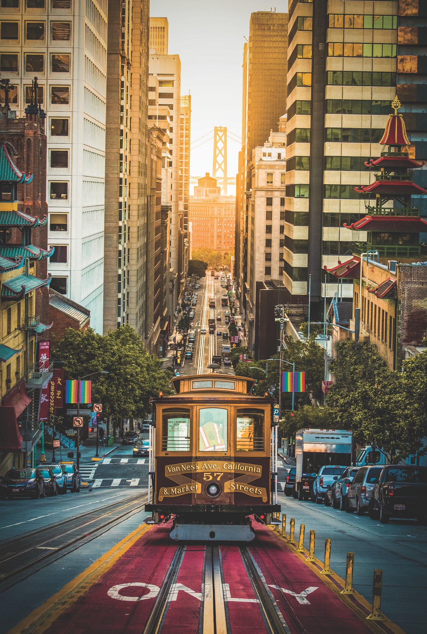 A photo of a cable car coming up the hill towards the camera with a sunrise and bridge in the background