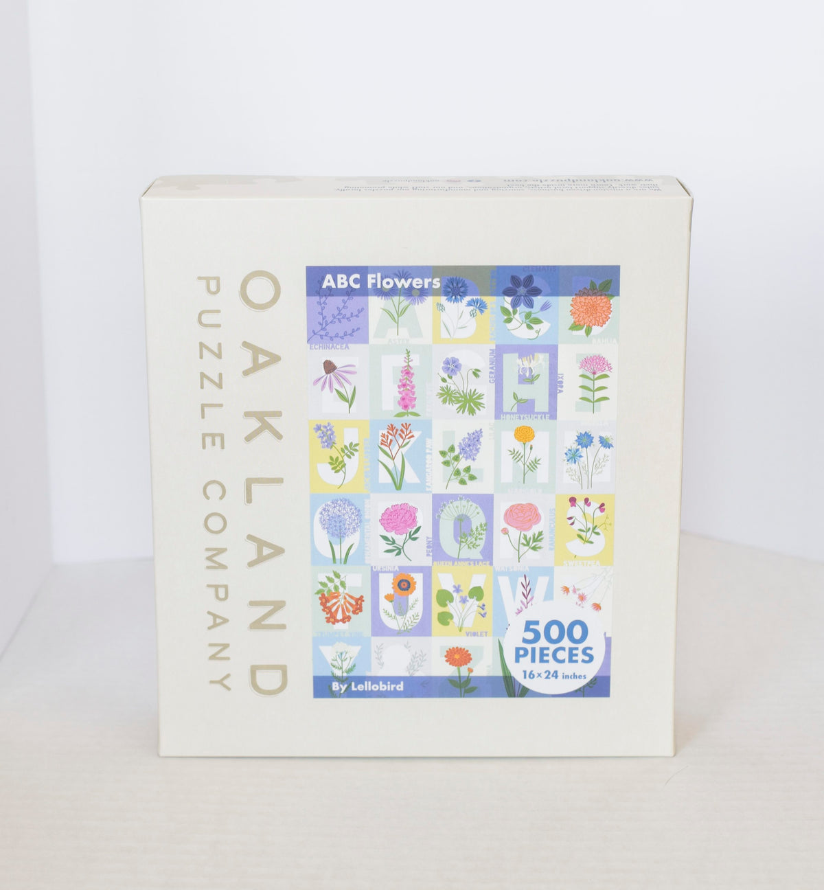 A jigsaw puzzle product box showing a pastel grid image of flowers over the alphabet with Oakand Puzzle Company branding.