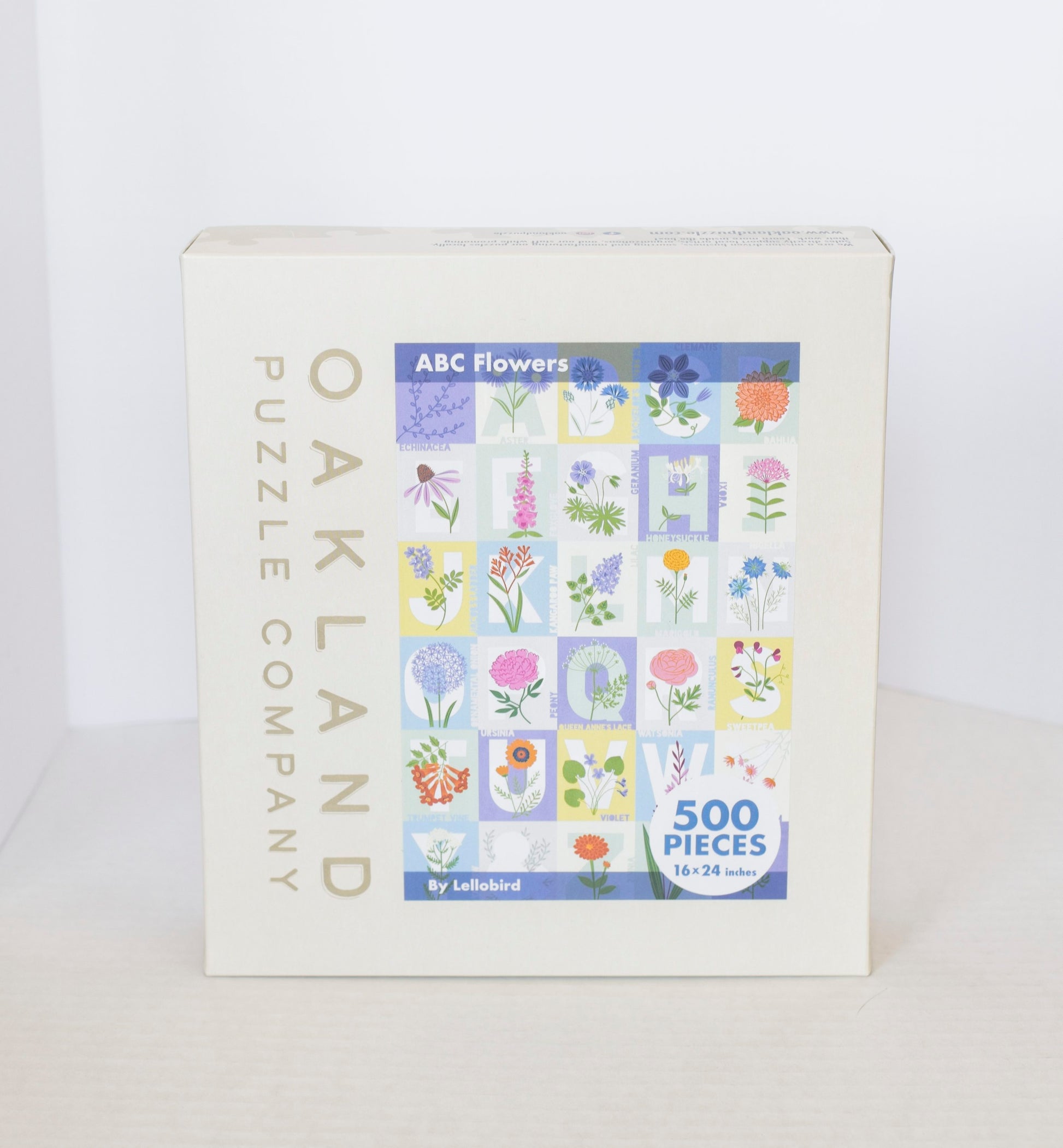 A jigsaw puzzle product box showing a pastel grid image of flowers over the alphabet with Oakand Puzzle Company branding.