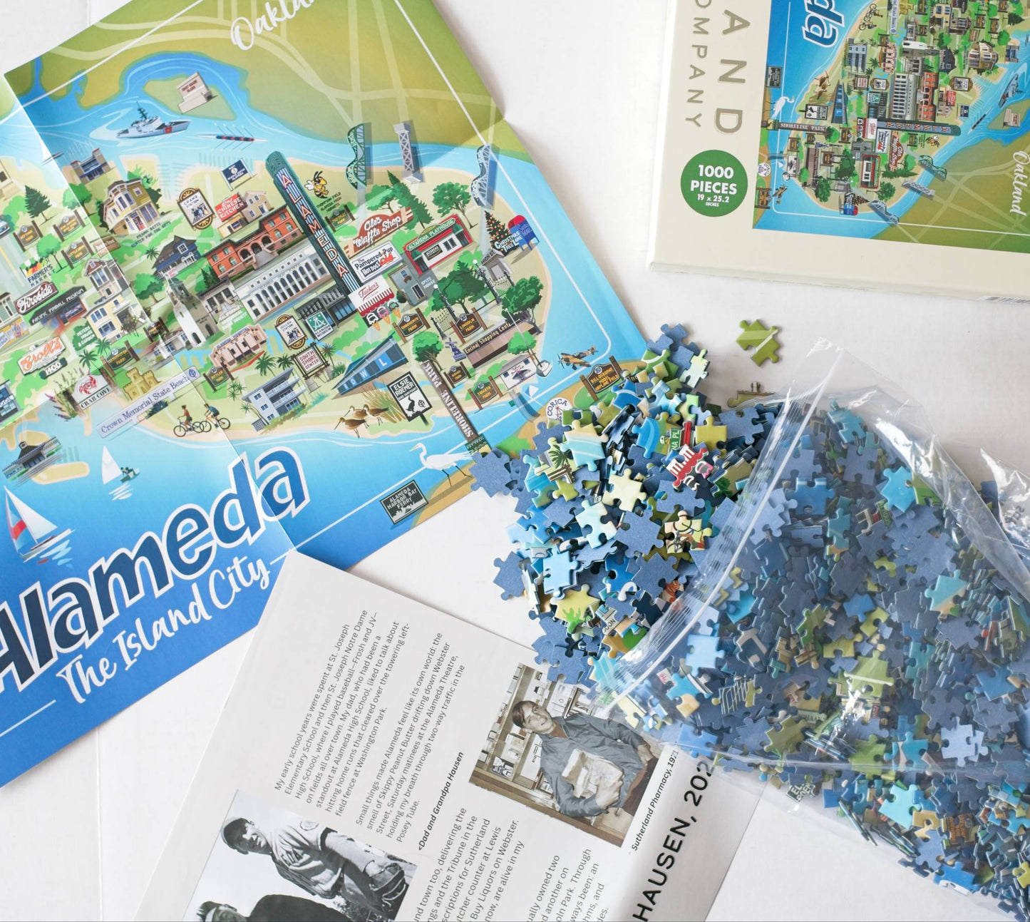 A 1000-piece jigsaw puzzle about Alameda, The Island City, shown with its illustrated box, a resealable bag of loose blue puzzle pieces, and printed inserts on a white background.