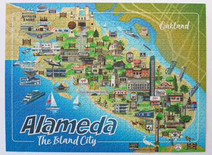 A completed jigsaw puzzle featuring a colorful illustrated map of Alameda, California, with the words 'Alameda The Island City' at the bottom and 'Oakland' in the upper right.