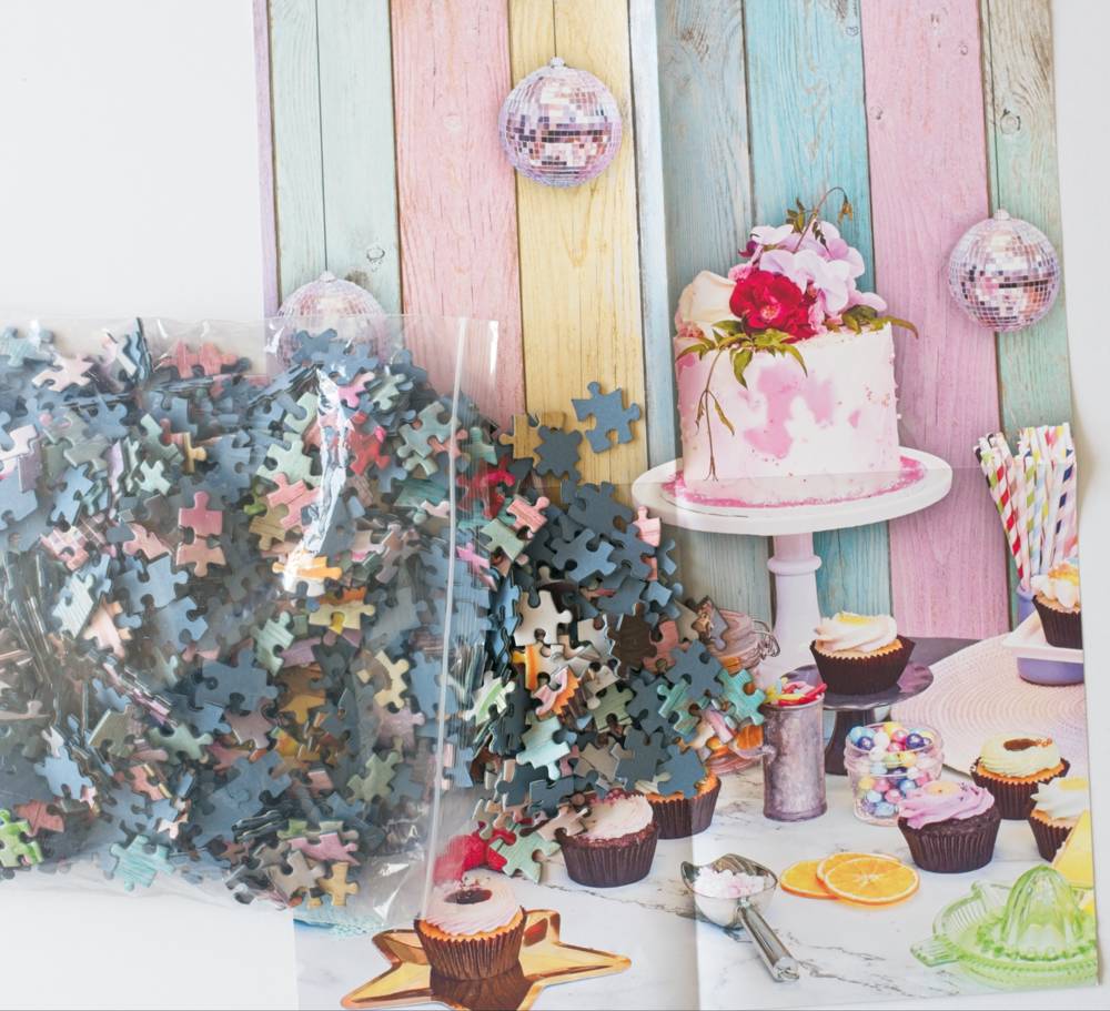 A styled party setup with a resealable bag of jigsaw puzzle pieces spilling onto the poster.