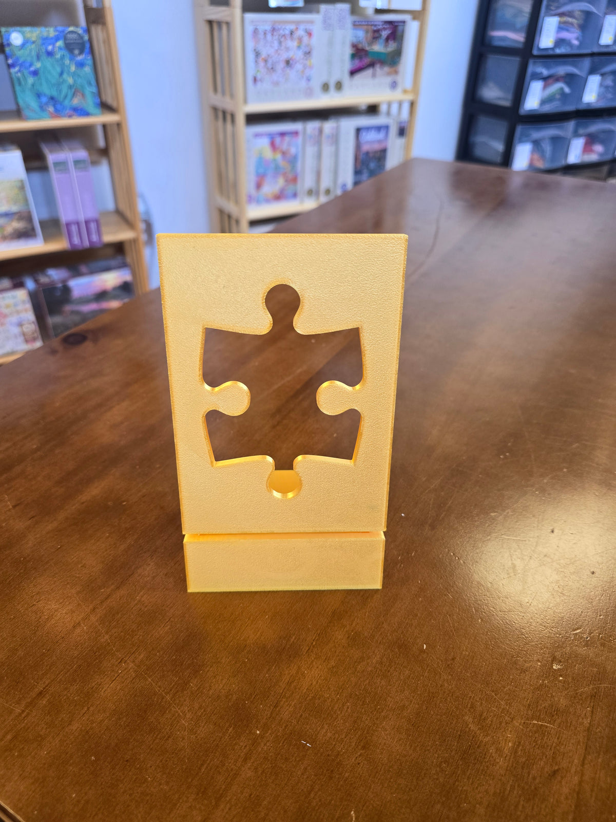 Gold colored boxtop stand with a puzzle piece cutout on a wooden surface with a blurred background
