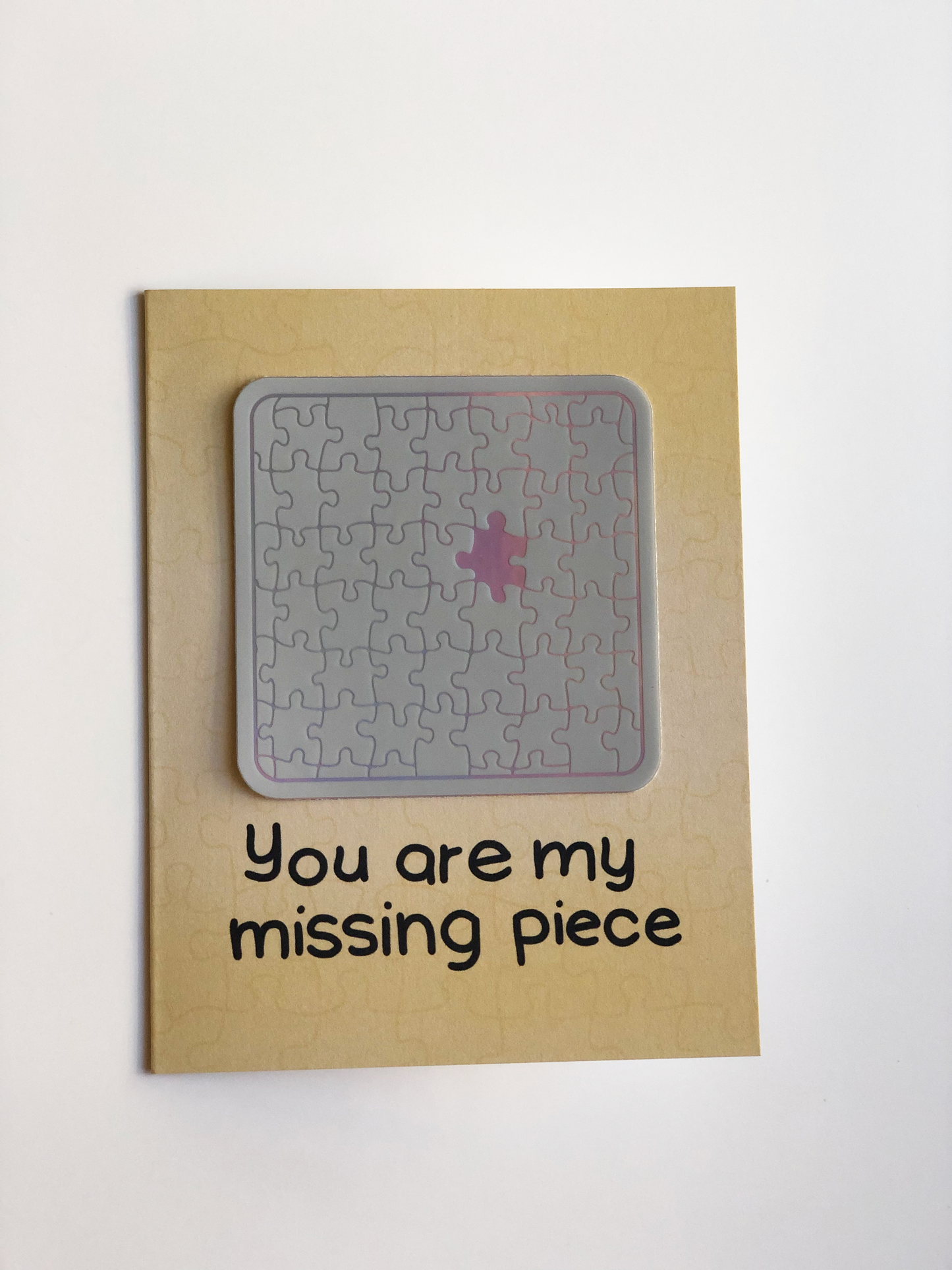 A greeting card with the text "You are my missing piece" and an irridescent sticker of a completed jigsaw puzzle with one piece missing.