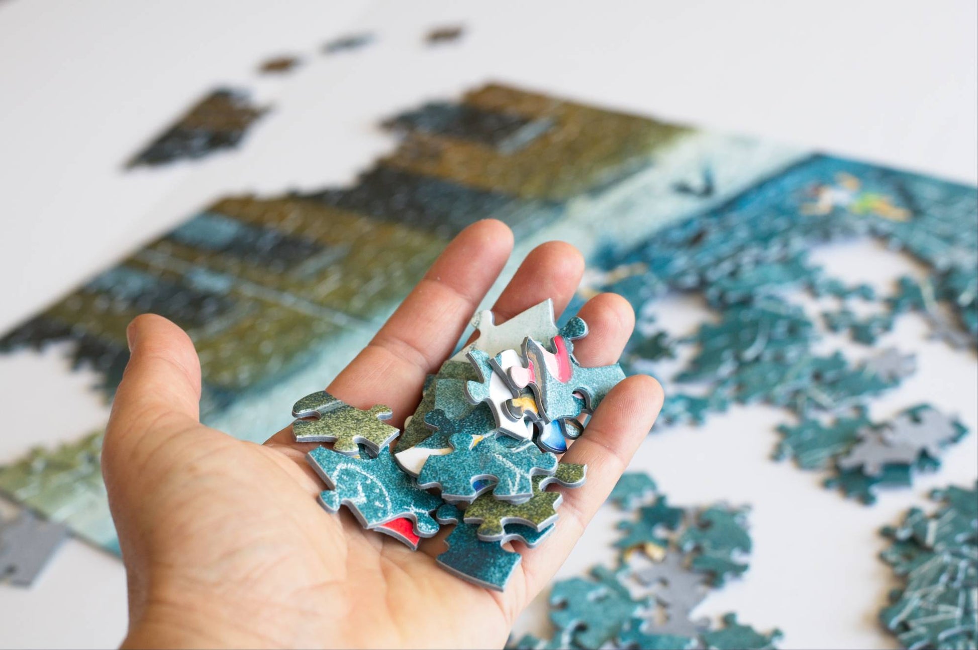A hand holding puzzle pieces with a partially completed jigsaw puzzle in the background.