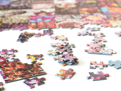 A stack of puzzle pieces with a few partially completed sections, and other pieces scattered around with a large section of completed puzzle all mostly various shades of red.