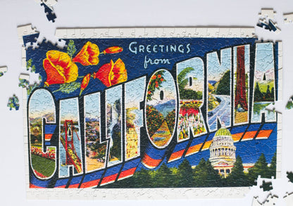 A partially completed puzzle featuring the image of a large letter vintage postcard with scenes from California