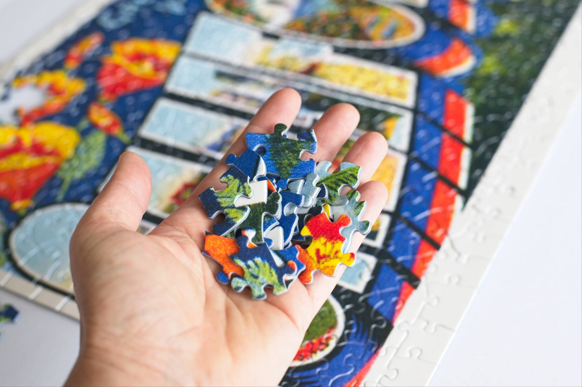 A hand holding colorful puzzle pieces with a partially completed jigsaw puzzle in the background.