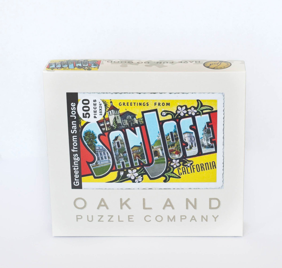 A box branded Oakland Puzzle Company labeled with a the image of a colorful vintage postcard reading Greetings from San Jose California 500 Pieces, 16x24"