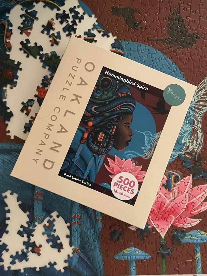 Jigsaw puzzle packaging with a colorful illustration of a person wearing a headwrap on a partially completed puzzle.