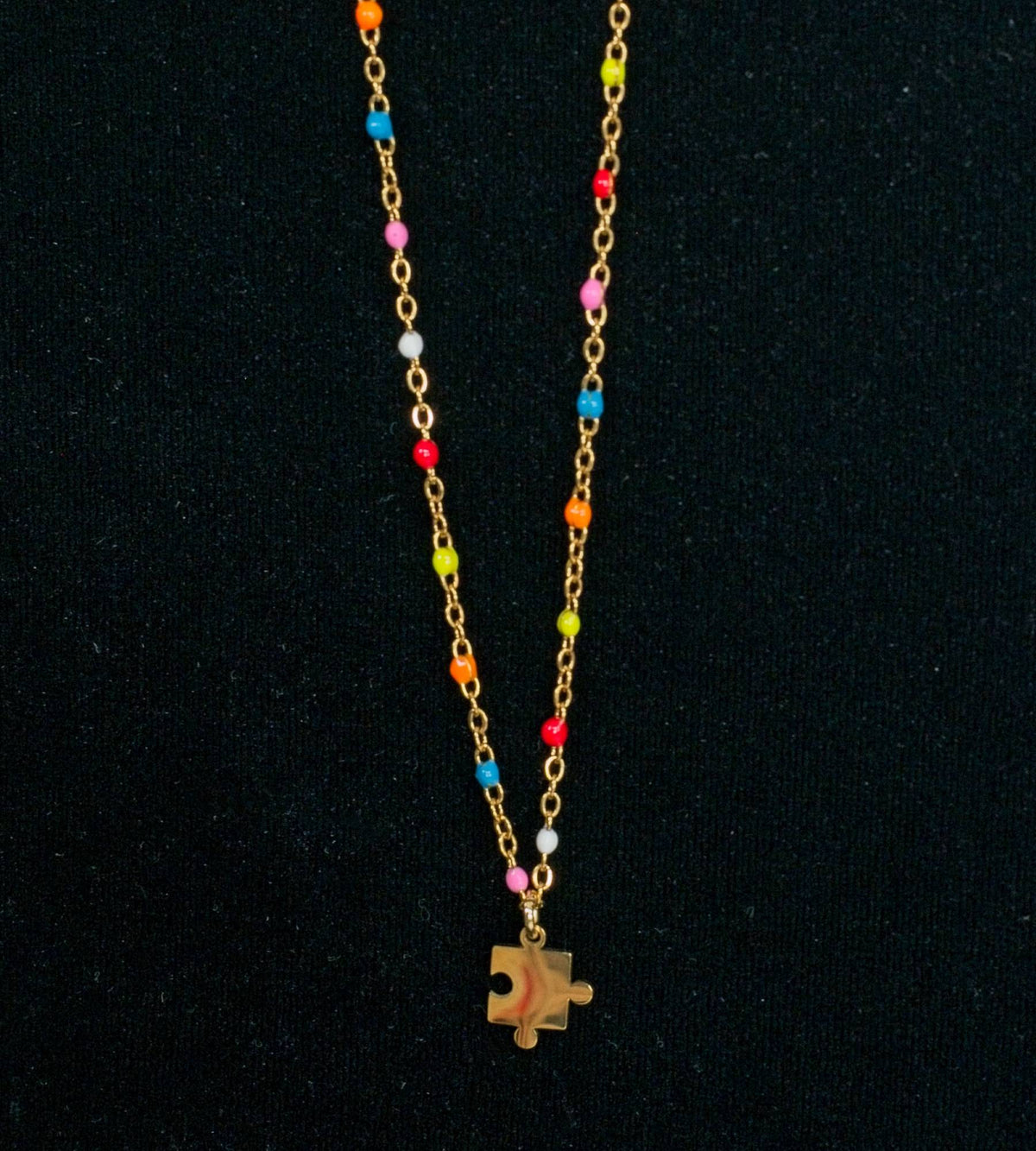Gold chain necklace with colorful beads and a puzzle piece charm on a black background