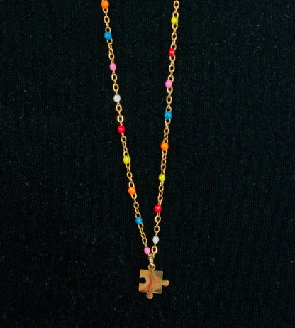 Gold chain necklace with colorful beads and a puzzle piece charm on a black background