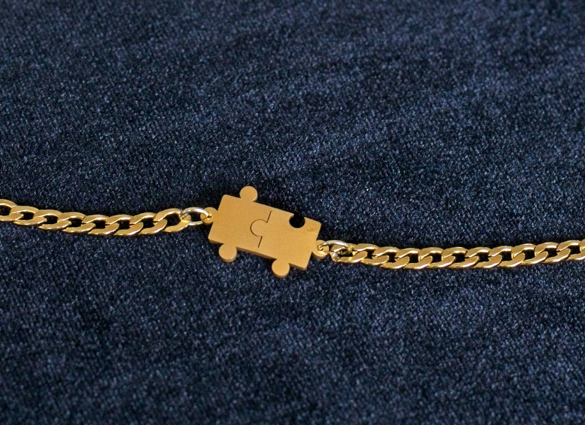 Gold curb chain bracelet with a puzzle piece connector charm on a black fabric background