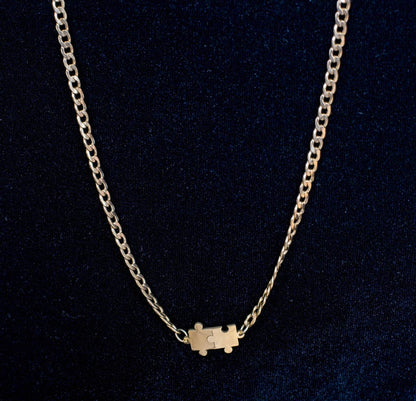 Gold curb chain necklace with a puzzle piece connector charm on a black background