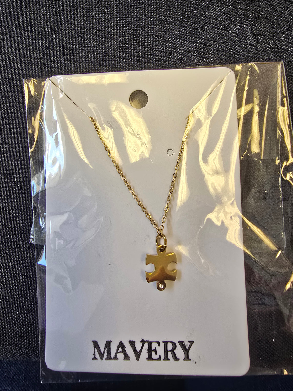Gold chain necklace with a puzzle piece pendant embedded with a stone on a Mavery branded card.