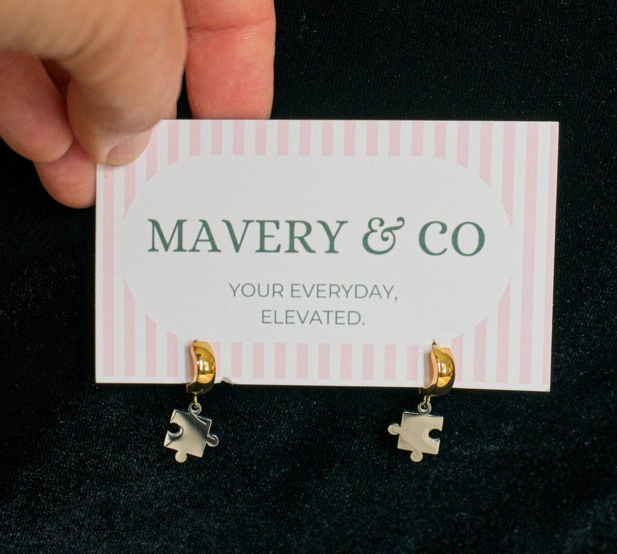 Pair of thick small gold hoop earrings with silver puzzle pieces dangling with a against a black background.