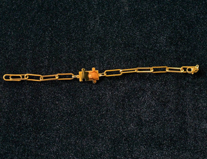 Gold paperclip chain bracelet with a puzzle piece connector charm on a dark textured background