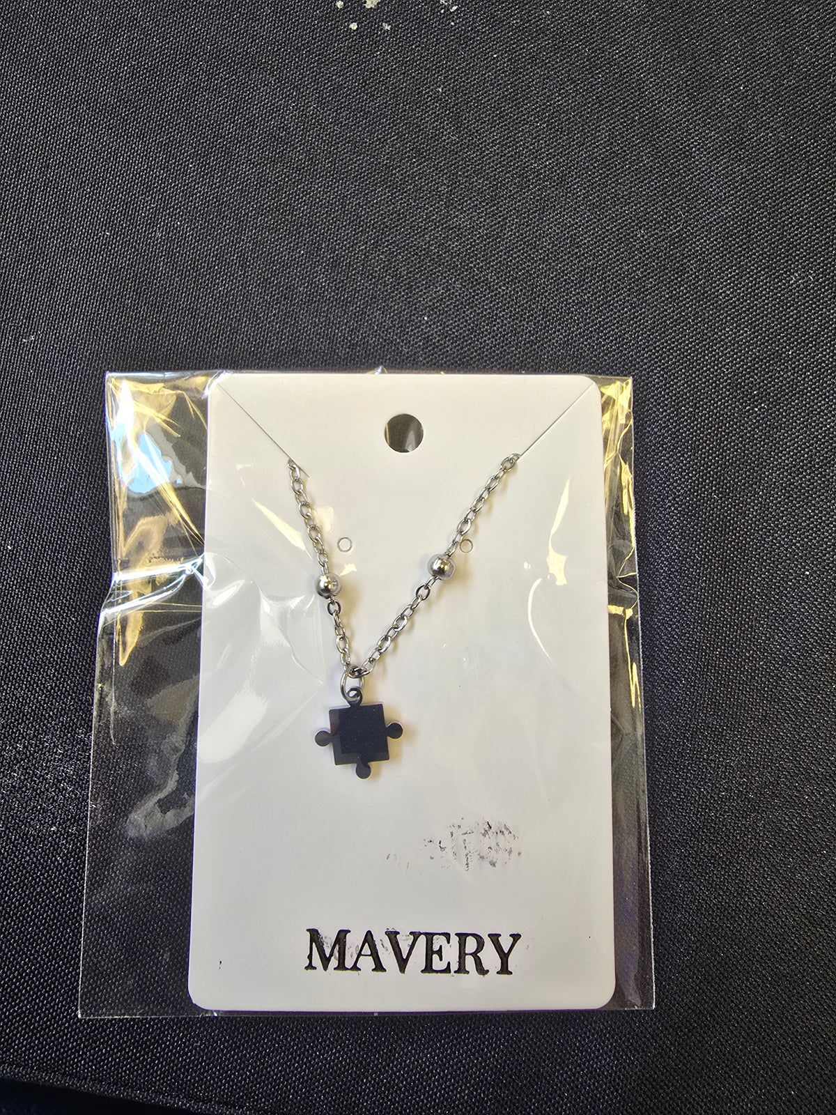 Silver beaded chain necklace with a puzzle piece pendant on a black background