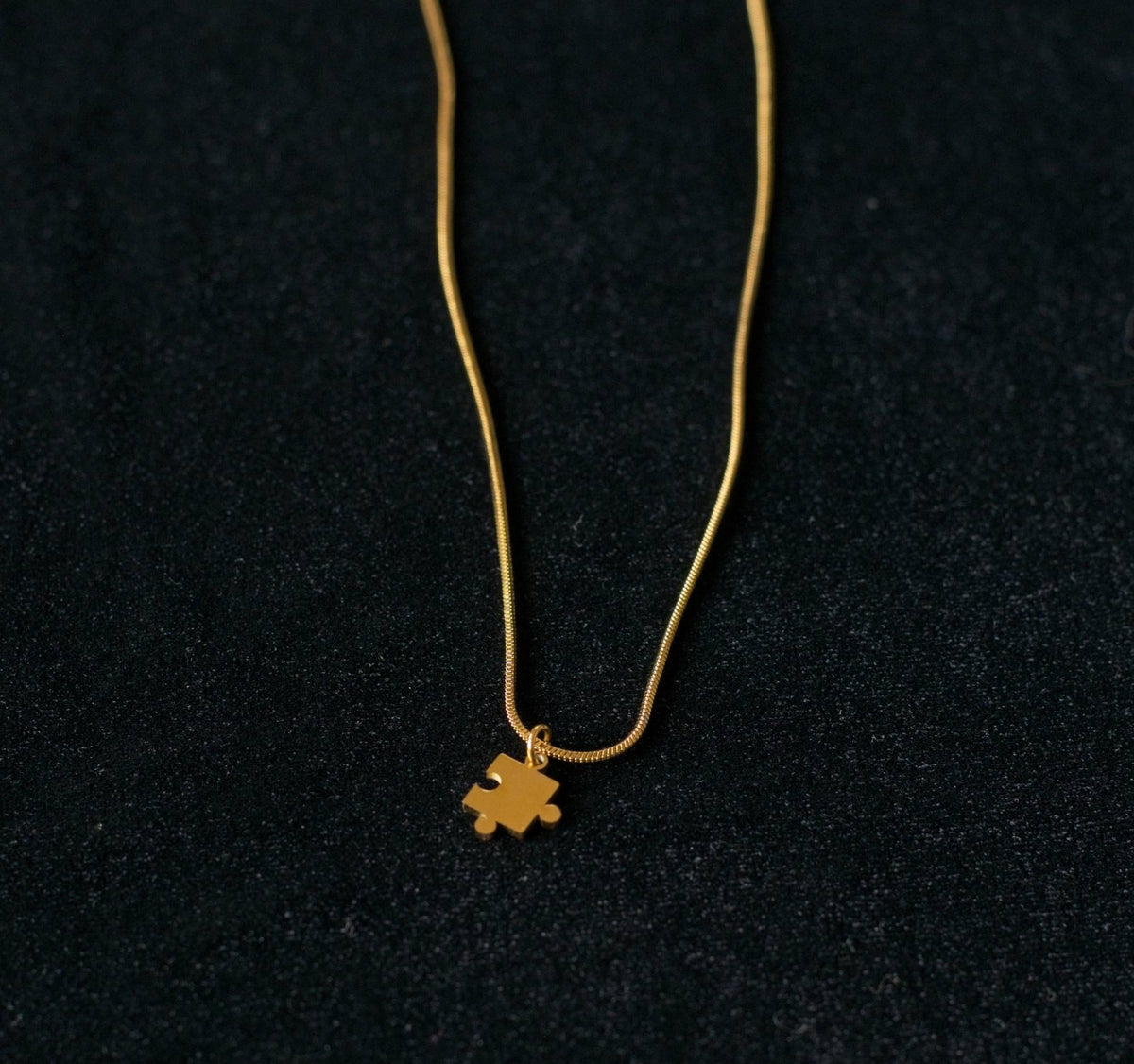 Gold snake chain necklace with a small pendant on a black background