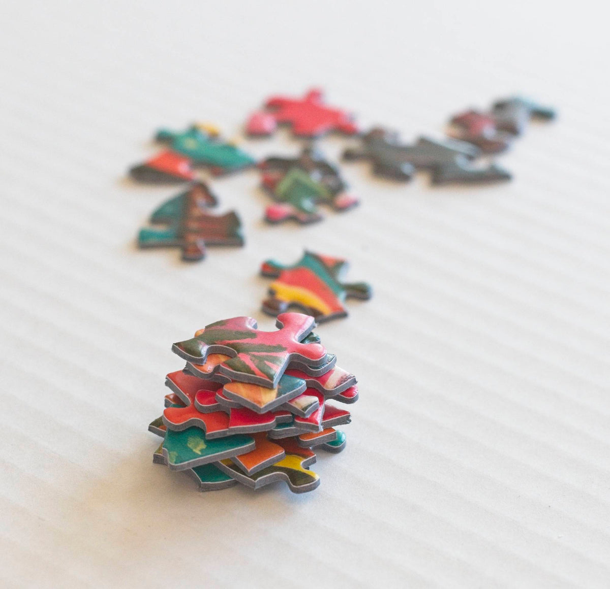 A stack of sturdy and colorful random shaped puzzle pieces with other scattered pieces out of focus in the background