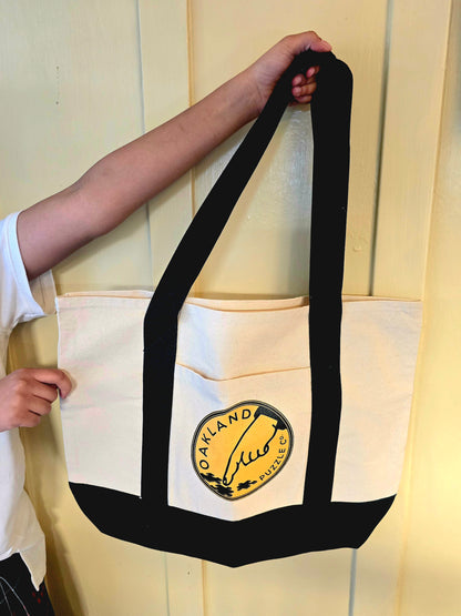 Person holding a beige tote bag with a logo against a light-colored wall