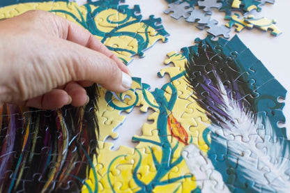 A hand placing a bright blue and yellow puzzle piece into a partially completed puzzle.