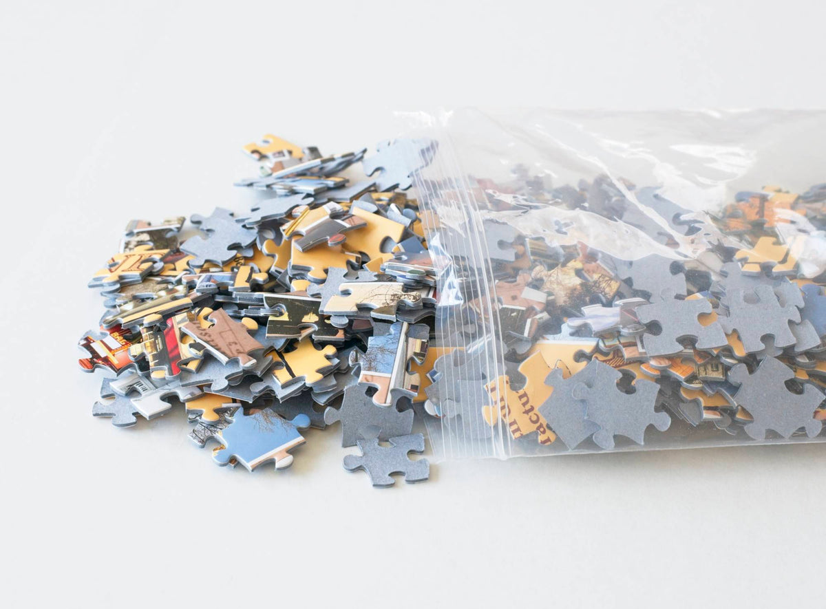 A resealable plastic bag with colorful jigsaw puzzle pieces made with blue board spilling from it. 