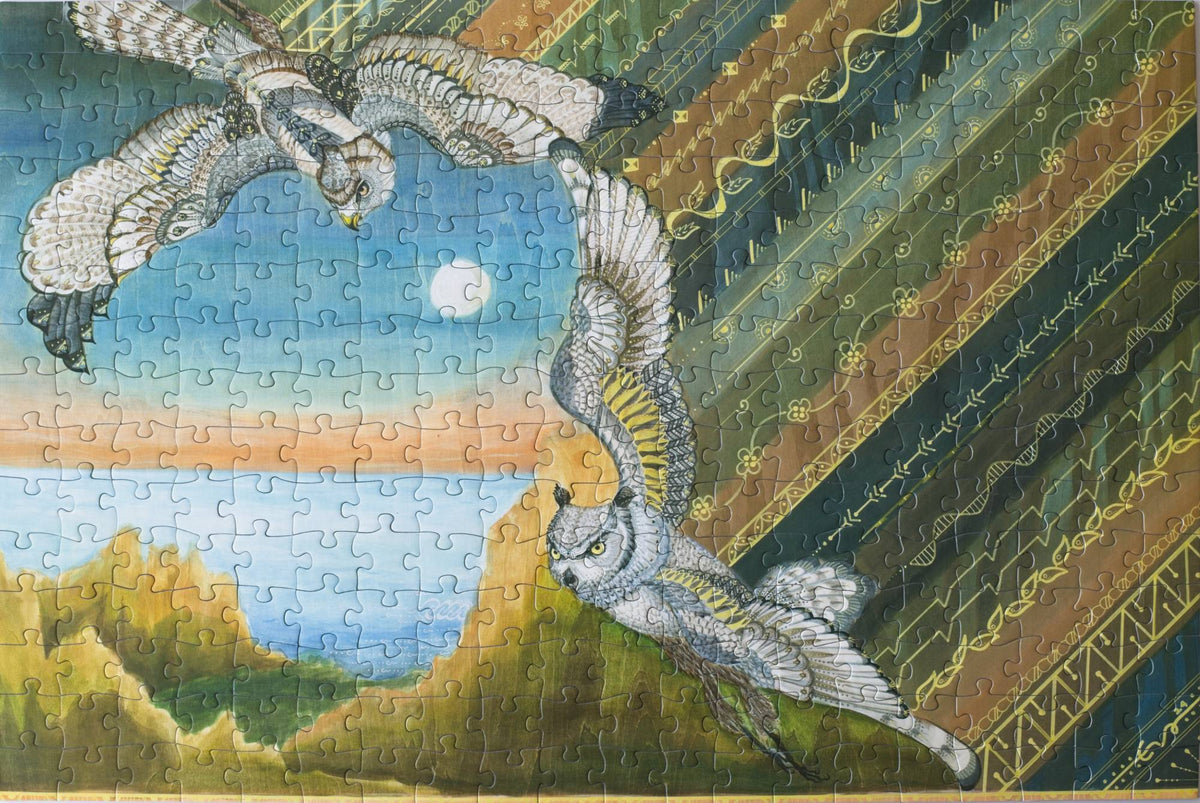 A completed jigsaw puzzle with a showing two raptors flying over a coastal landscape with a batik pattern on one side
