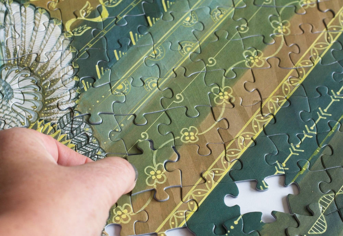Hand holding a puzzle piece with a decorative pattern on a partially completed puzzle.