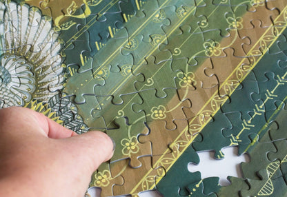 Hand holding a puzzle piece with a decorative pattern on a partially completed puzzle.