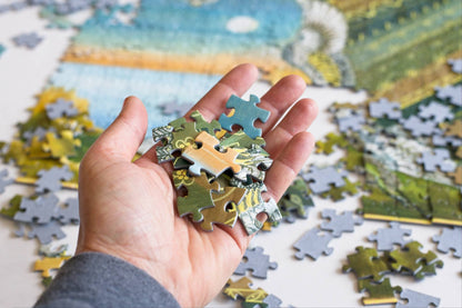 Hand holding puzzle pieces with a partially completed puzzle in the background