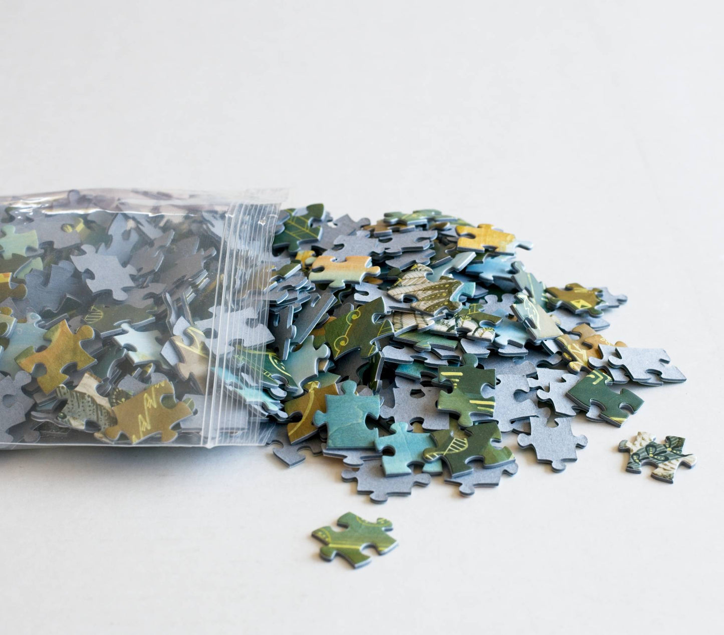 A resealable bag spilling out a pile of puzzle pieces on a white background