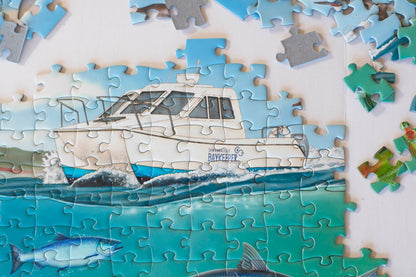A completed section of jigsaw puzzle showing a boat marked San Francisco Baykeeper on the water with fish below. Puzzle pieces area scattered above.